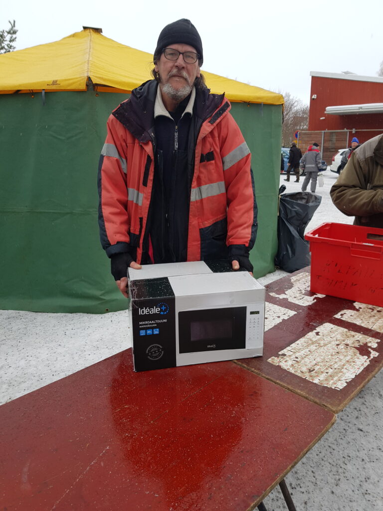 Mies seisoo vihreän teltan edessä palkintomikroaaltouunin kanssa.