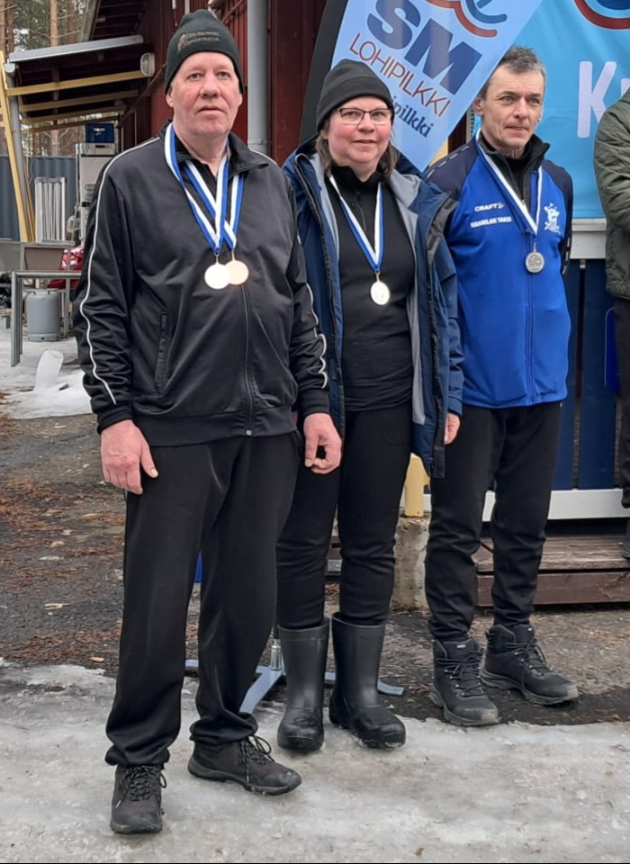 Kolme henkilö poseeraa rivissä mitallit kaulassa